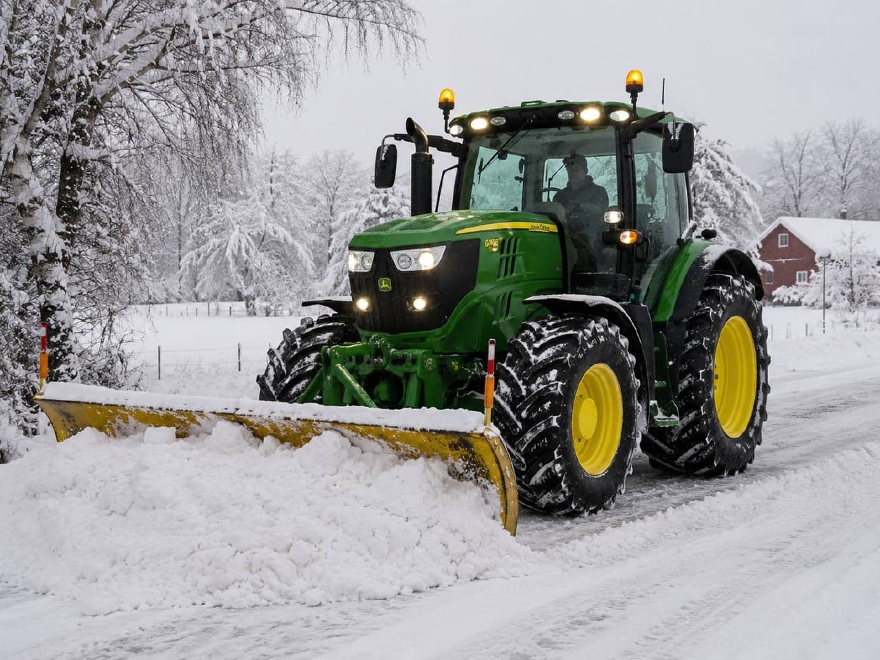 Traktor med brøyteskjær rydder snø på vinterveg